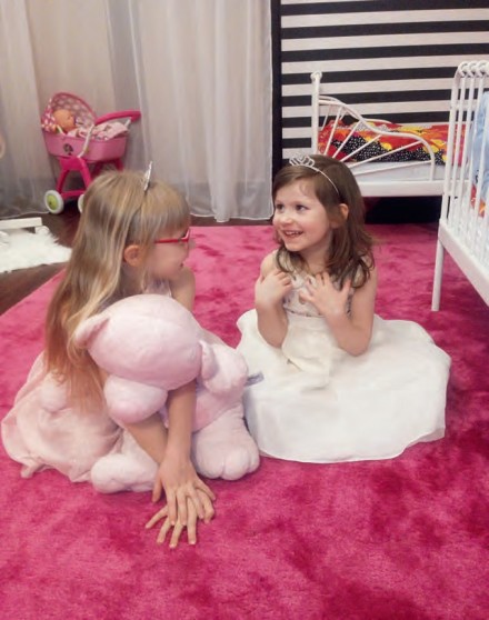 Zdj 2. Małe księżniczki w trakcie zabawy. Ciepły, duży dywan sprzyja dziecięcym aktywnościom. 